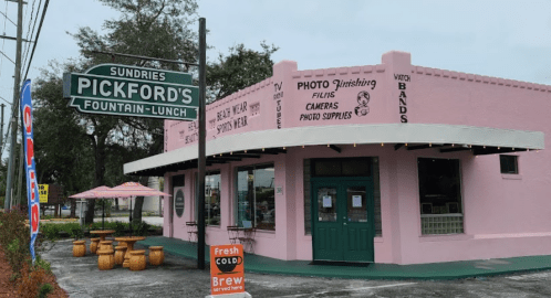 A pink building with a sign reading "Pickfords Fountain Lunch" and outdoor seating, featuring a photo supply shop.