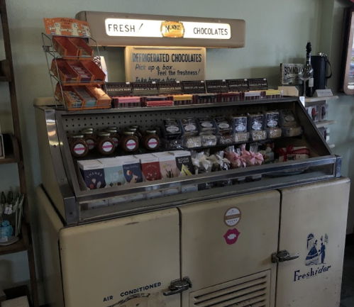 A vintage ice cream cart displaying various chocolates and treats under a sign that reads "Fresh Chocolates."