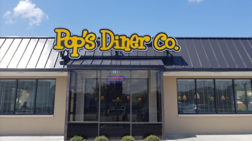 Exterior of Pop's Diner Co. with a bright sign and an "Open" neon light in the window. Clear blue sky above.