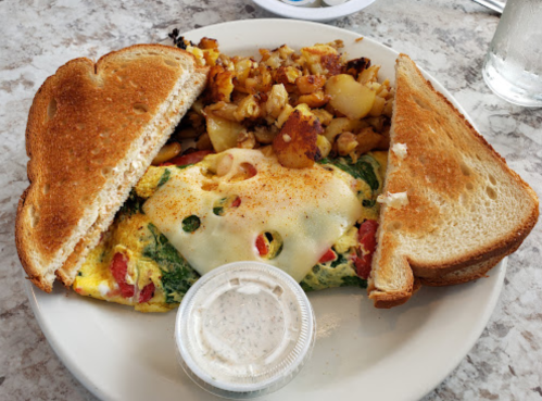 A plate with an omelet topped with cheese, served with toast, seasoned potatoes, and a side of dipping sauce.