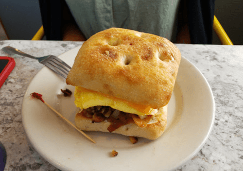 A sandwich on a plate with a fluffy egg, bacon, and cheese, served on a toasted ciabatta roll.