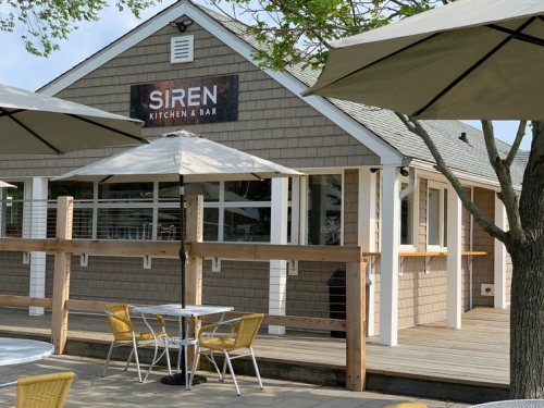 Exterior view of Siren Kitchen & Bar, featuring a wooden deck, outdoor seating, and a sign on a shingled building.