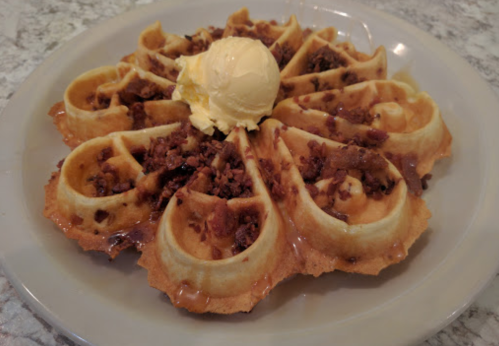 A plate of waffles topped with ice cream and crumbled toppings, drizzled with syrup.