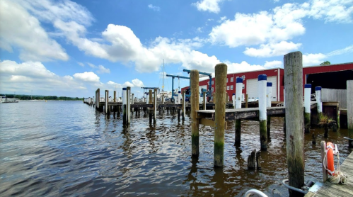 A serene waterfront scene with wooden docks, boats, and a blue sky dotted with clouds.