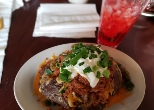 A loaded baked potato topped with chili, cheese, sour cream, and green onions, alongside a glass of red drink.