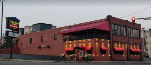 A red brick restaurant with a red awning and outdoor seating, located at a street corner with a traffic light.