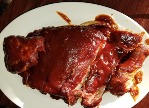 A plate of tender, barbecued ribs coated in a rich, dark sauce, served on a white platter.