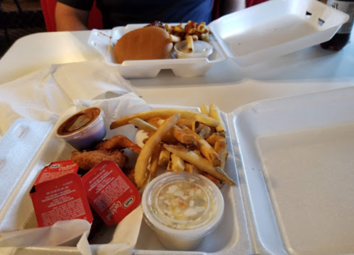 A takeout meal featuring fried chicken, fries, dipping sauces, and a burger in a styrofoam container.