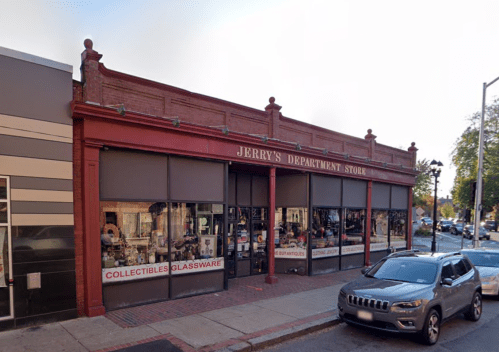 Exterior of Jerry's Department Store, featuring large windows displaying collectibles and glassware, with parked cars nearby.