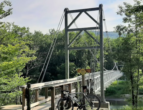 A suspension bridge surrounded by trees, with a bike parked on the wooden walkway.