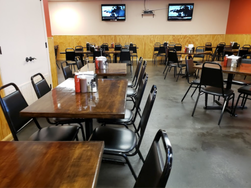 A spacious restaurant interior with wooden tables, black chairs, and two TVs on the wall.