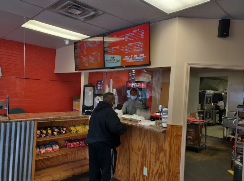 A customer orders food at a counter with a menu display in a casual eatery, while staff prepare food in the background.