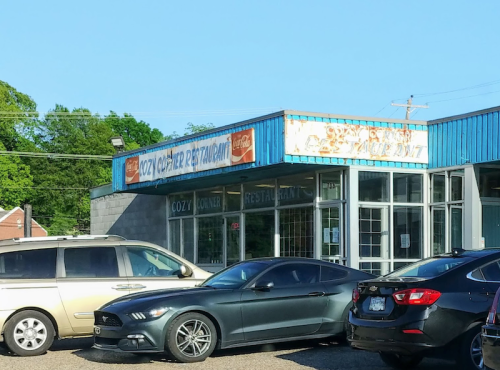 Exterior of Cozy Corner Restaurant with parked cars in front and a clear blue sky above.