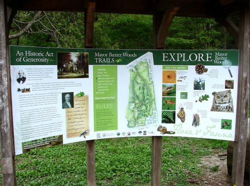 Informational sign about Mayor Baxter Woods, featuring trails, flora, fauna, and park rules.