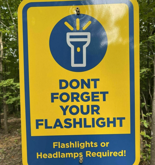 Sign reminding visitors to bring a flashlight or headlamp, featuring an icon of a flashlight.