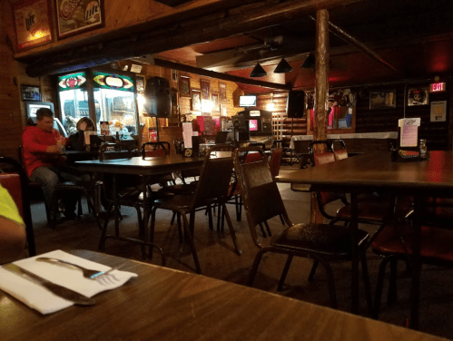 A dimly lit restaurant interior with empty tables, a few patrons, and a jukebox in the background.