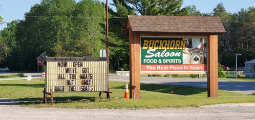 Sign for Buckhorn Saloon, announcing it's open and serving pizza, with a humorous note about limited meat options.