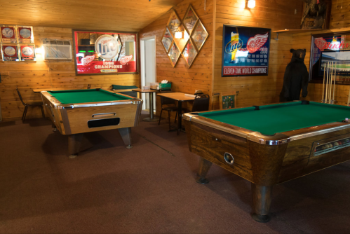 A cozy game room featuring two pool tables, wooden walls, and sports memorabilia.