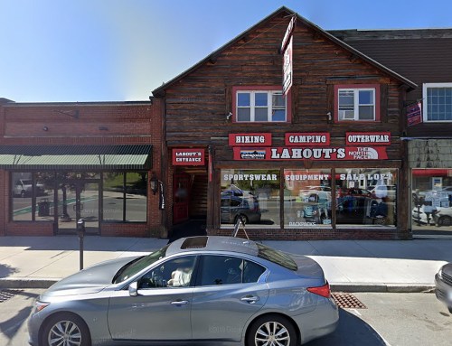 A wooden storefront with signs for Lahout's hiking, camping, and outdoor gear, alongside a parked car.