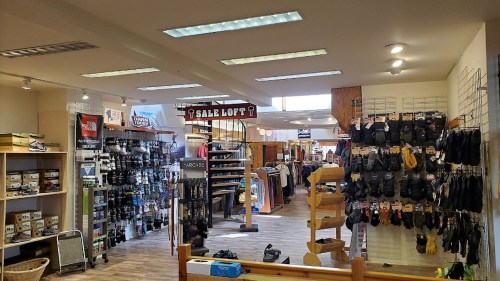 Interior of a retail store showcasing various outdoor gear and clothing, with a spiral staircase and sale signs.