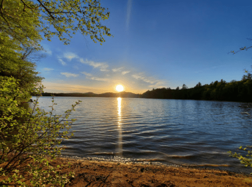 Sunset over a calm lake, with trees framing the scene and gentle waves reflecting the golden light.