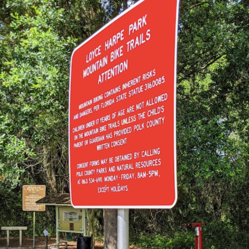 Red sign at Loyce Harpe Park warns of mountain biking risks and outlines consent requirements for children under 17.