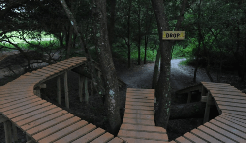 Wooden pathways winding through trees, with a sign reading "DROP" visible in a forested area.