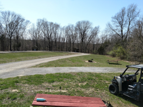 A scenic view of a gravel road winding through a wooded area, with a picnic table and an off-road vehicle in the foreground.
