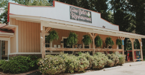 Exterior of Gina Belle's Restaurant featuring a wooden porch and hanging plants, surrounded by greenery.
