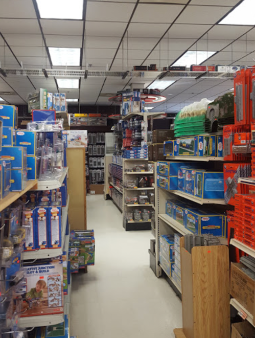 A narrow aisle in a store filled with shelves of various toys and model kits, brightly lit with overhead lights.