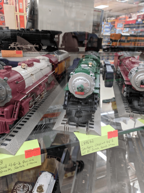 Display of model trains in a glass case, featuring various steam locomotives with colorful details and labels.