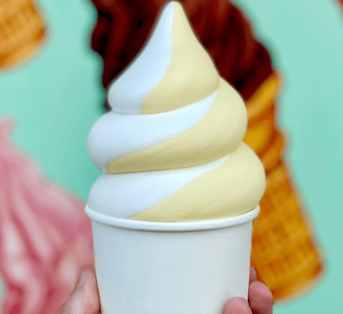 A hand holding a soft-serve ice cream cone with swirls of yellow and white against a colorful background.