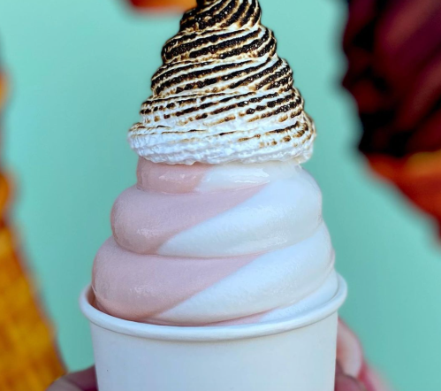 A close-up of a soft-serve ice cream cone with pink and white swirls, topped with toasted meringue.