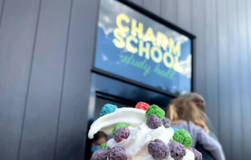 A close-up of a colorful ice cream treat with sprinkles in front of a building sign that reads "Charm School."