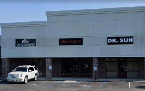 Exterior view of a commercial building with three storefronts: "dhi," "BREAKOUT," and "DR. SUN," plus a white SUV parked outside.