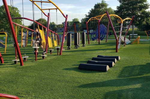 A colorful playground with climbing structures and soft turf, featuring children playing and exploring various equipment.