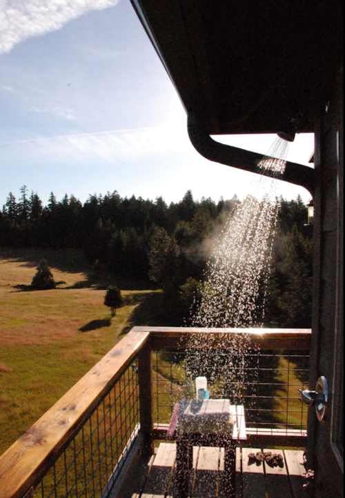 A balcony with a water spout pouring water onto a table, surrounded by a scenic view of trees and fields.