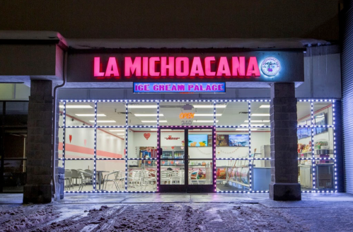 Brightly lit ice cream shop "La Michoacana" with festive lights, snow-covered ground, and a welcoming entrance.