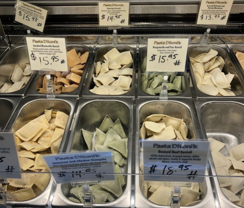 A display of various types of fresh pasta in metal trays, with price tags for each variety.