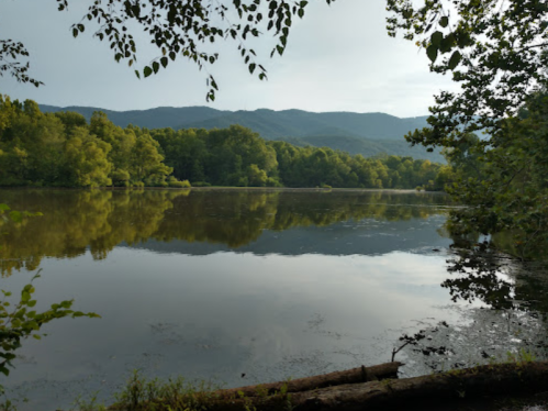 A serene lake surrounded by lush trees and mountains, reflecting the calm water under a cloudy sky.