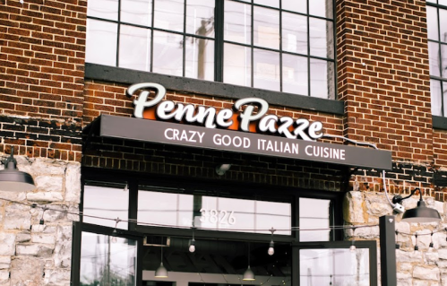 Sign for "Penne Pazze" restaurant featuring the tagline "Crazy Good Italian Cuisine" on a brick building.