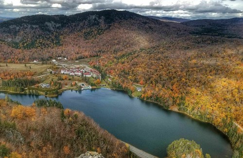 Aerial view of a lake surrounded by autumn foliage and a small village nestled in the mountains.