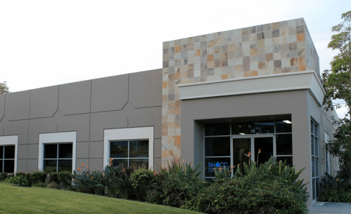 Modern building exterior with stone accents, large windows, and landscaped greenery in front.