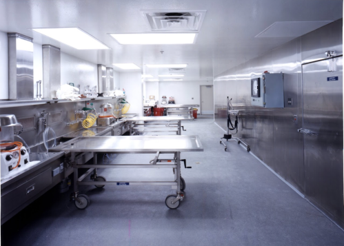 A clean, stainless steel kitchen with work tables, equipment, and bright overhead lighting.