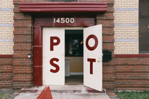 Open double doors of a brick building with large letters spelling "POST" above the entrance.