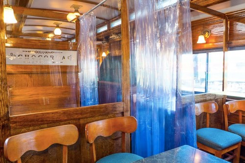 Interior of a cozy café with wooden decor, featuring transparent plastic curtains and blue upholstered chairs.