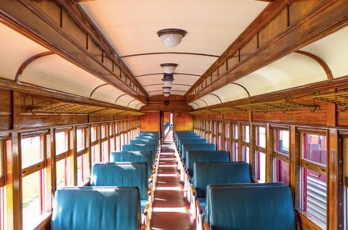 Interior of a vintage train car featuring wooden paneling and green upholstered seats, with sunlight streaming through windows.