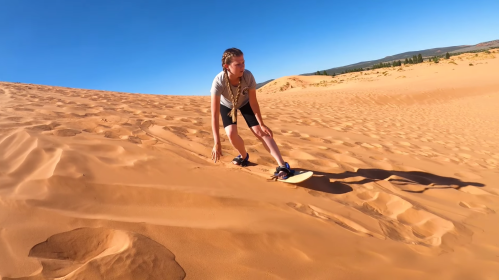 A person sandboarding down a sandy dune under a clear blue sky.