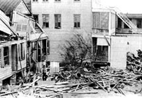 Black and white photo of damaged buildings and debris, indicating destruction from a disaster.