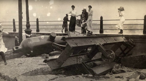 Historic photo of a large, overturned object on a pier, with people walking nearby, capturing a moment of curiosity.